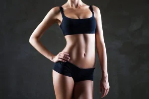 A woman in a black bikini outfit displaying her well toned arms after having Arm Liposuction.