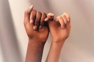 Following fat grafting, the hands of a man and a woman tying their small fingers together display smooth, wrinkle-free hands.