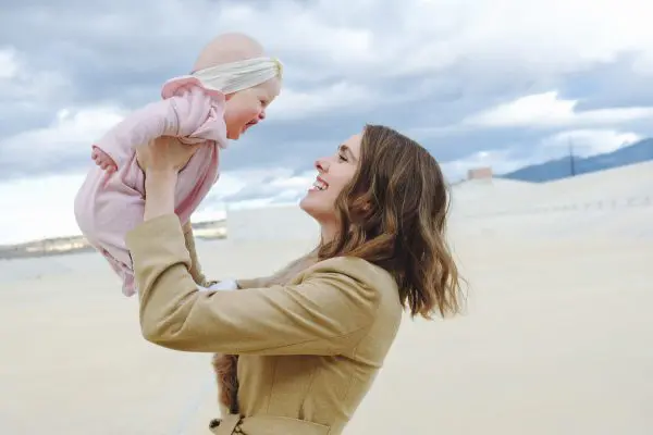 A mummy is playing with her toddler and they are both grinning at each other.